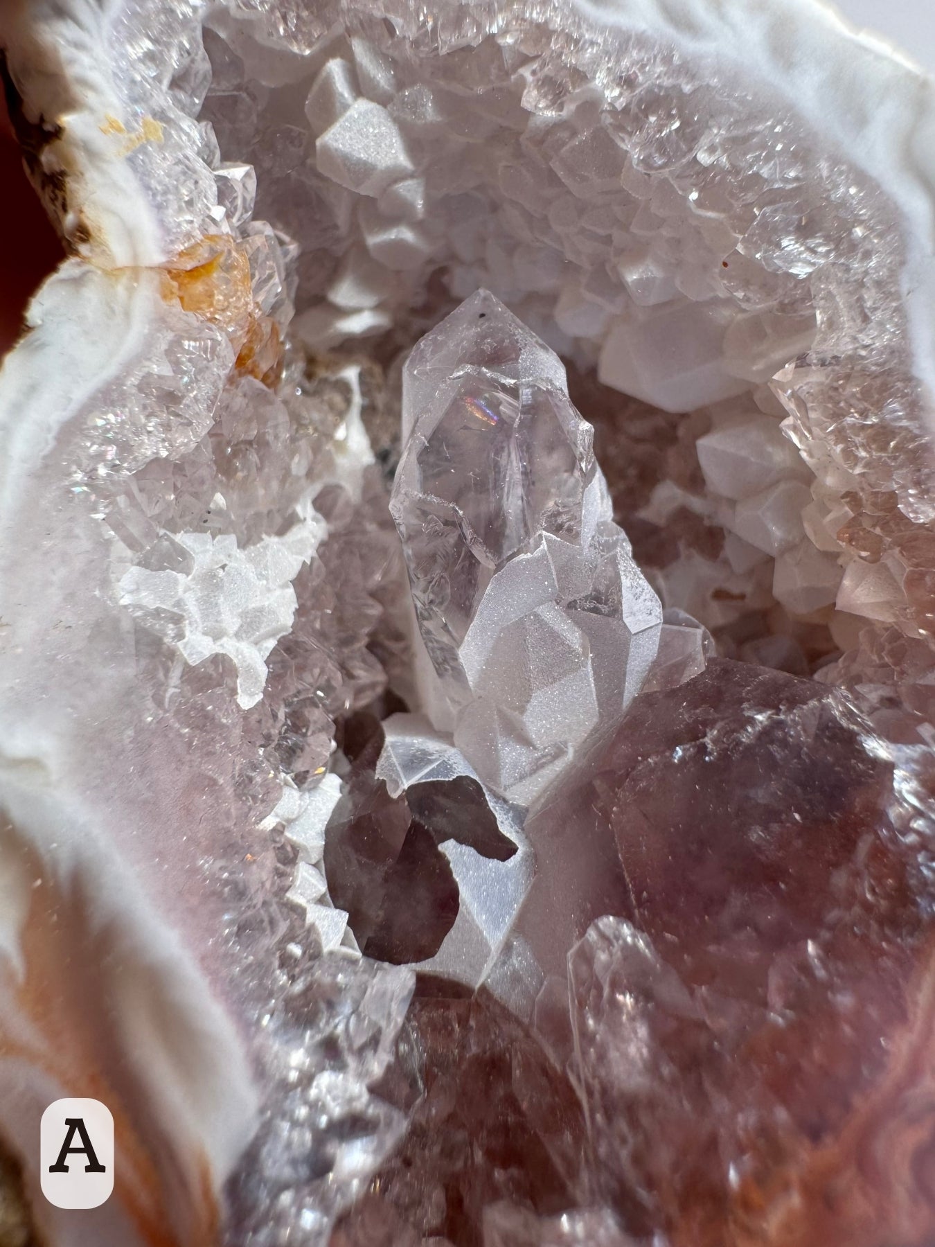 Option A: Detail of the quartz cluster in the center of the geode, well-formed quartz points with a small rainbow inside one, and partially coated in sugary white overgrowth.