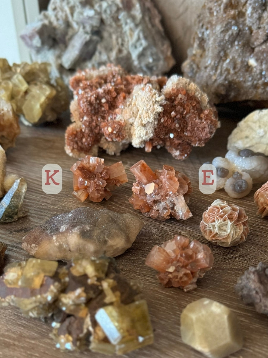 Two sputnik aragonites on a mineral shelf. The one on the left is labeled K and has good radiating form, and the one on the right is labeled E with more irregular form.