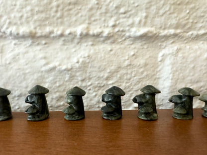 A more distant view of dark green mushroom trios lined up in a row, showing more variations in natural coloration, with lighter and darker mottling.