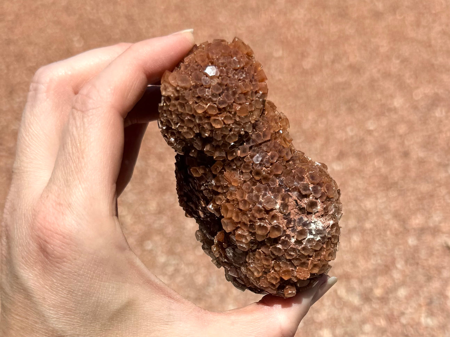 Side view of the piece, appearing more like a sphere atop an oval. There are well-formed crystals on this side with some opaque light red-brown mineral between them near the bottom.