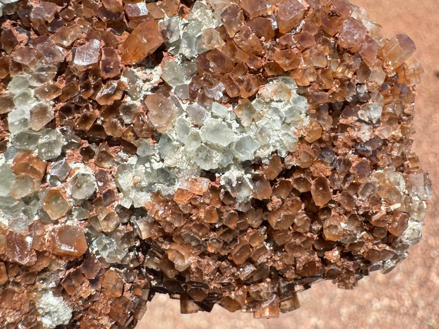 Detail of the surface, with a lot of the pseudo-hexagonal crystals flattened into diamond or parallelogram shapes. There is good translucency. There is an opaque white and red mineral spotting the piece between crystals