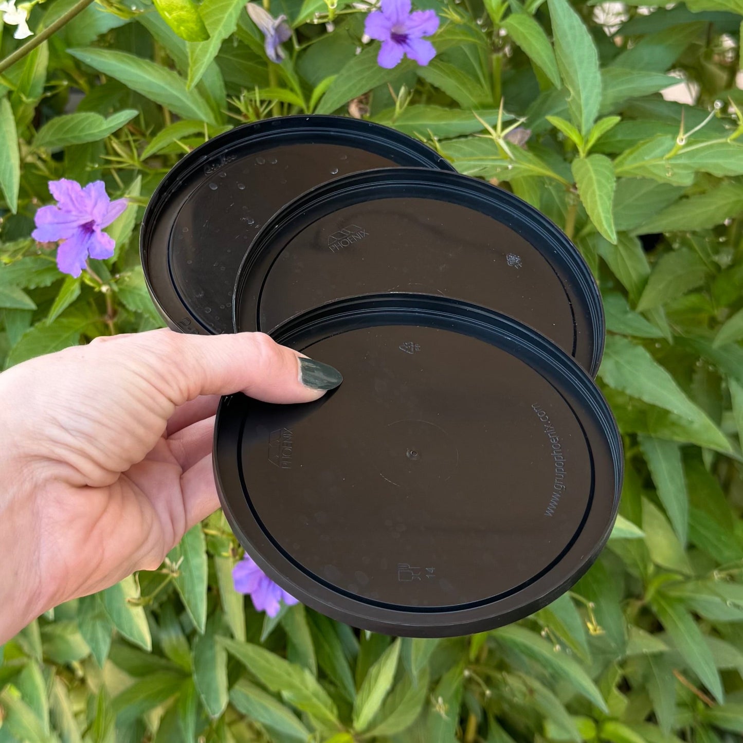 A hand holding three black plastic lids, they are thin and flat.