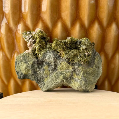 One side of a flat roughly rectangular specimen, largely green and gray matrix with the top ridge covered in epidote crystals.