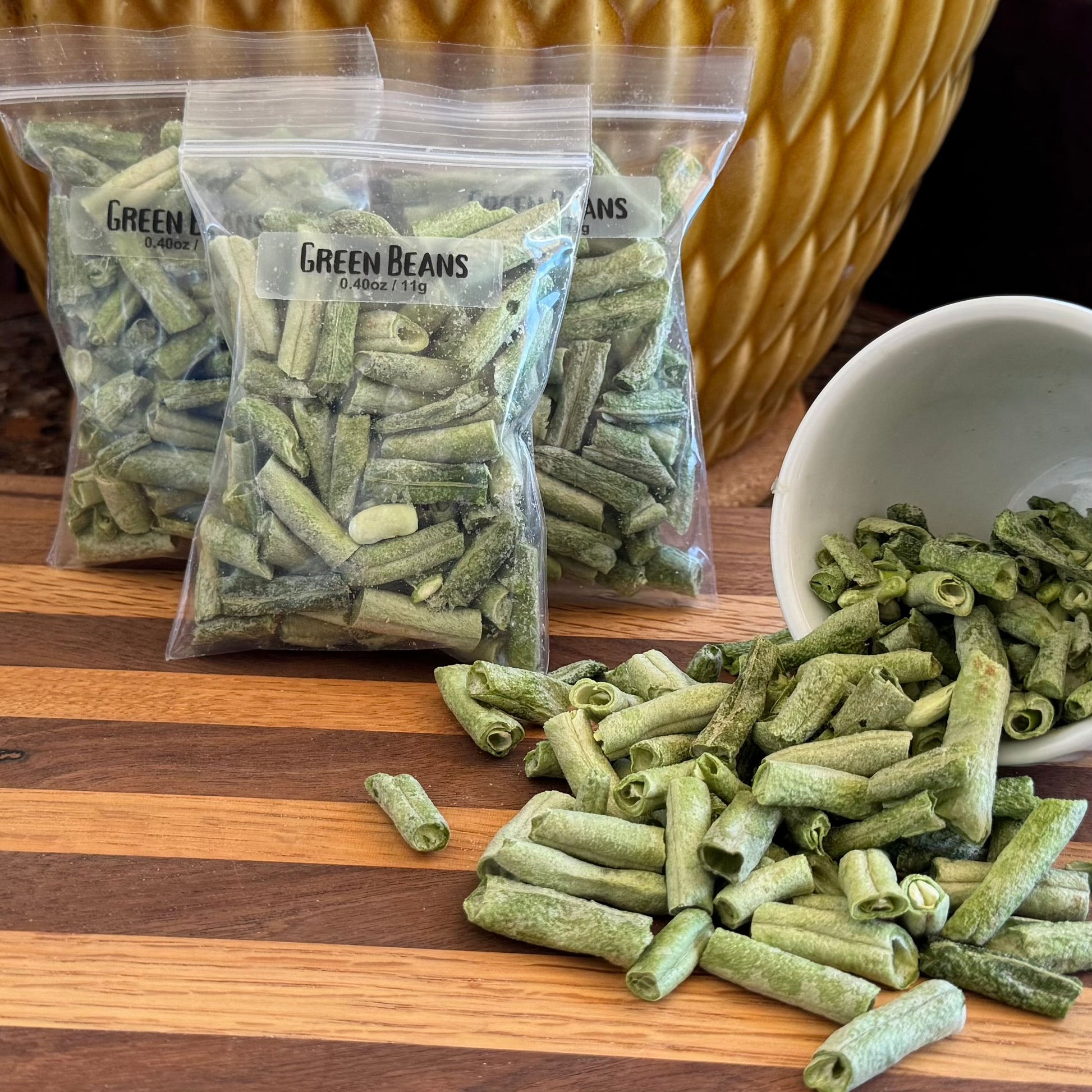 Several bags filled with dried green beans, labeled "Green Beans 0.40oz / 11g," with a small bowl to the right spilling dried green beans