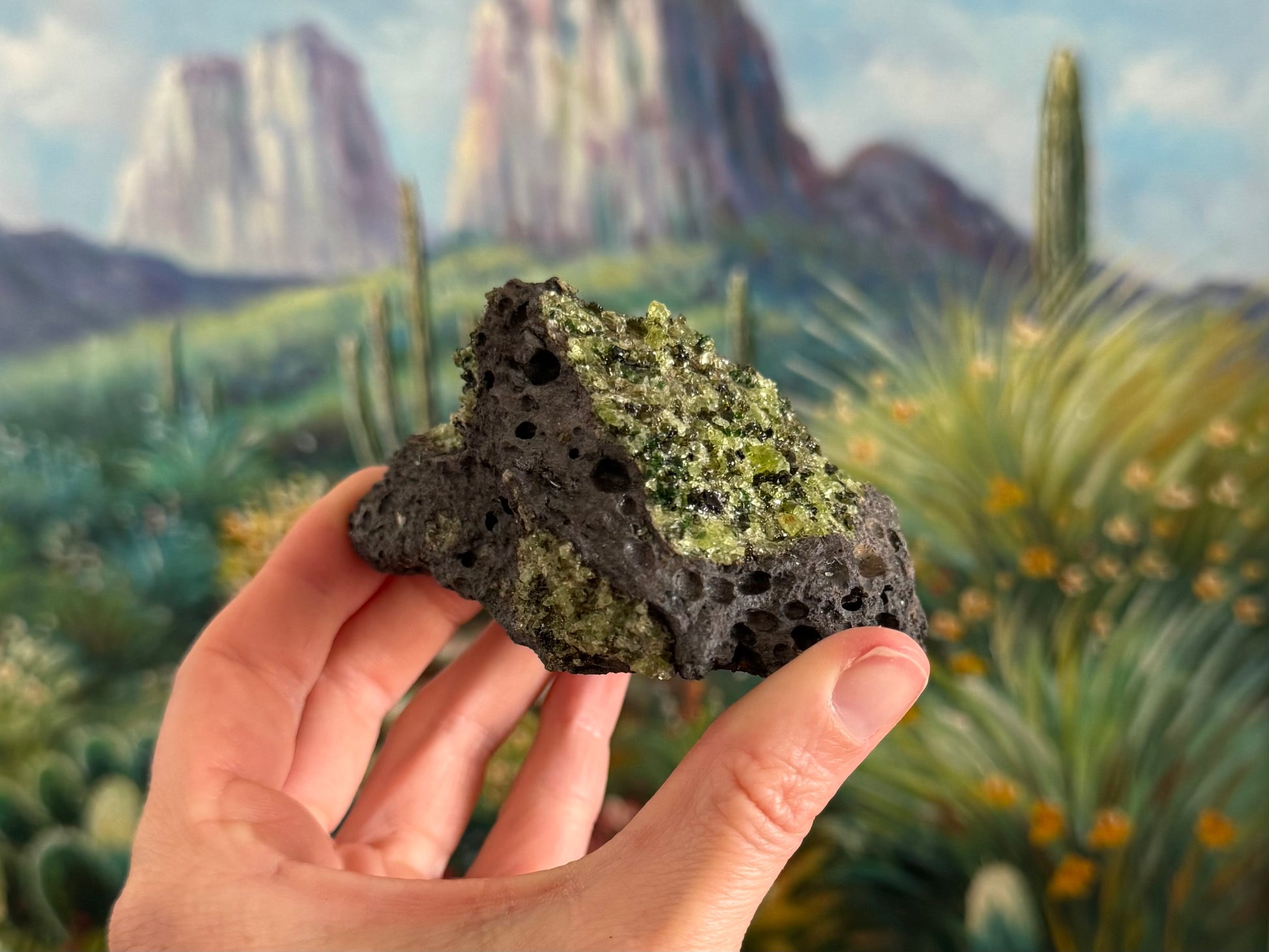 A rough wedge-shaped chunk of dark gray porous volcanic basalt with a large patch of peridotite on top and a smaller patch with darker crystals on the base.