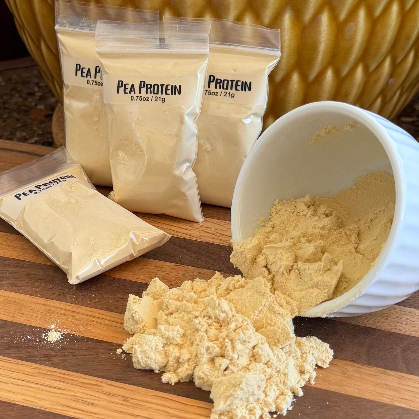 Several bags filled with light cream powder, labeled "Pea Protein 0.75oz / 21g," with a small bowl to the right spilling protein powder