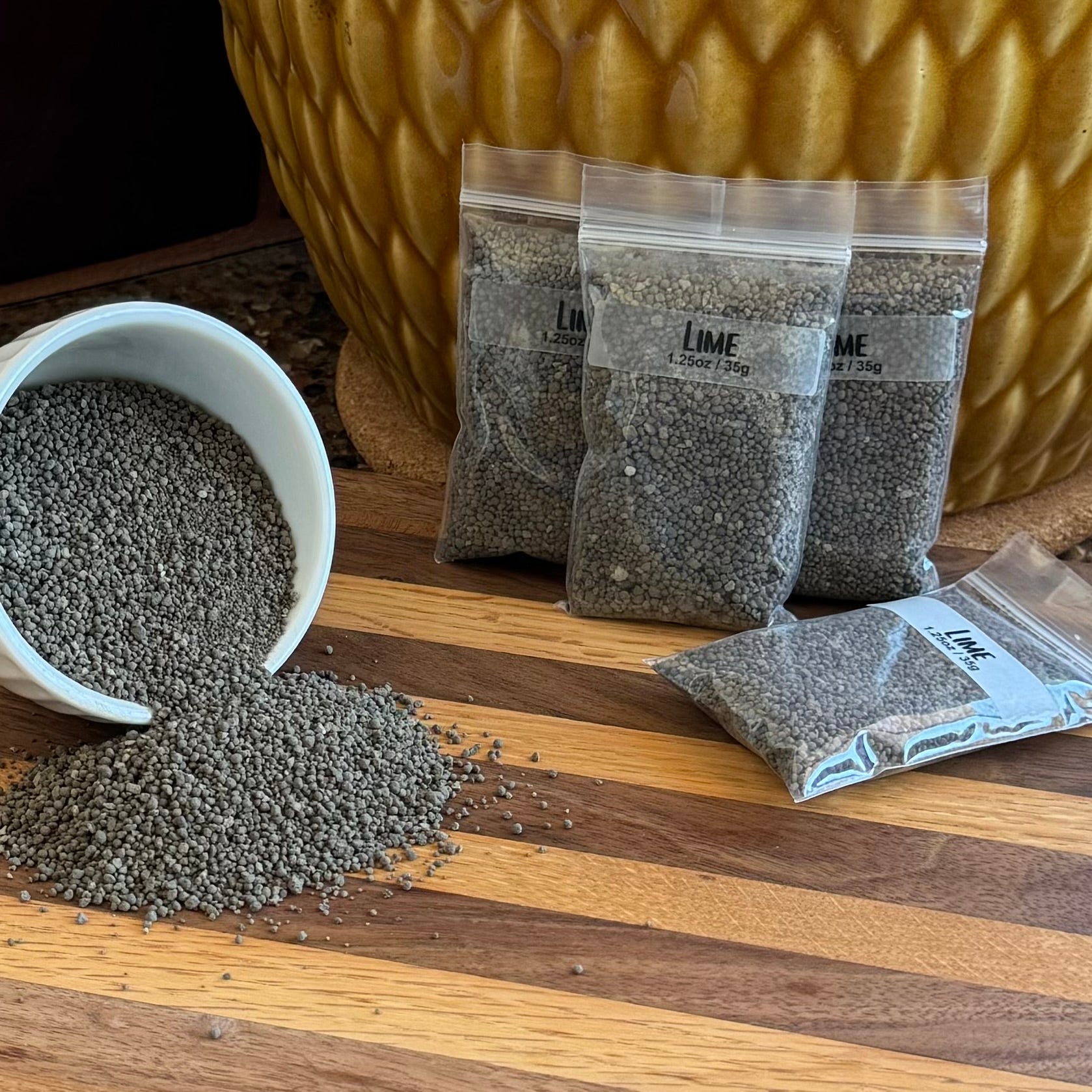 Several small plastic ziploc bags labeled "Lime 1.25oz / 35g." To the left is a small white bowl on its side spilling small dark gray pellets.