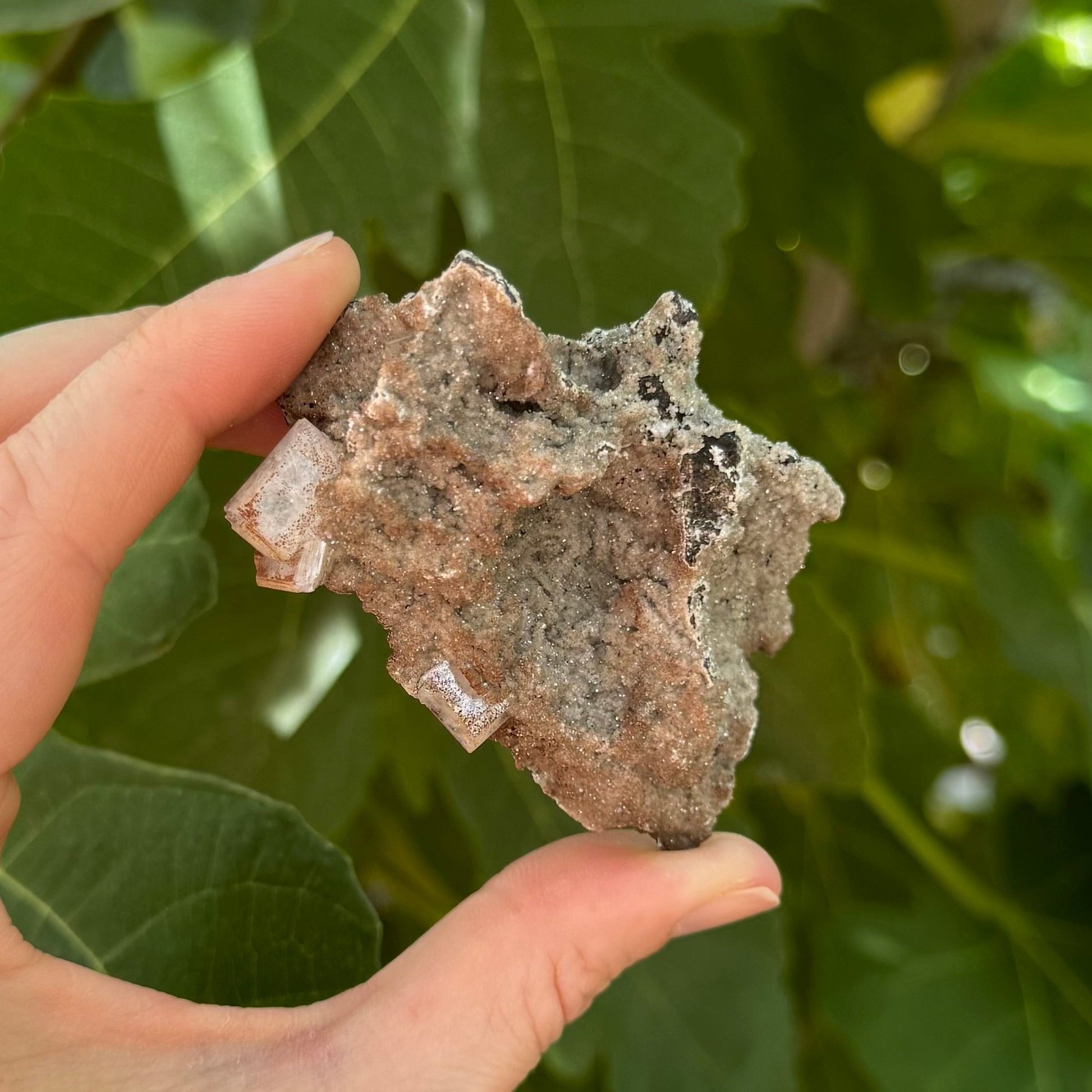 The piece held between thumb and finger for scale, showing the back covered in glittering druzy formed in almost squiggly lines like pasta.