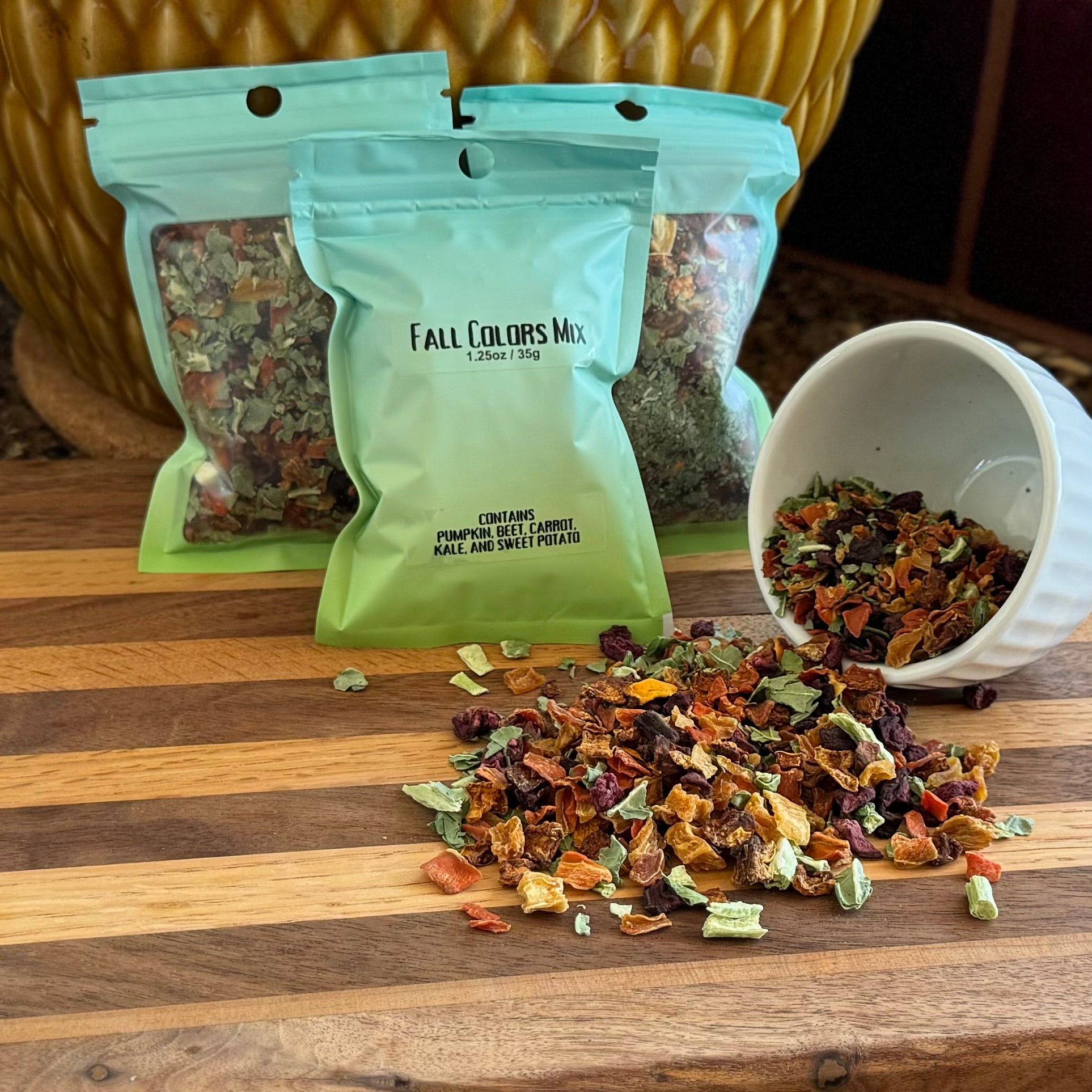 Several bags filled with a mix of dried vegetables, labeled "Fall Colors Mix 1.25oz / 35g," with a small bowl to the right spilling the dried vegetable mix