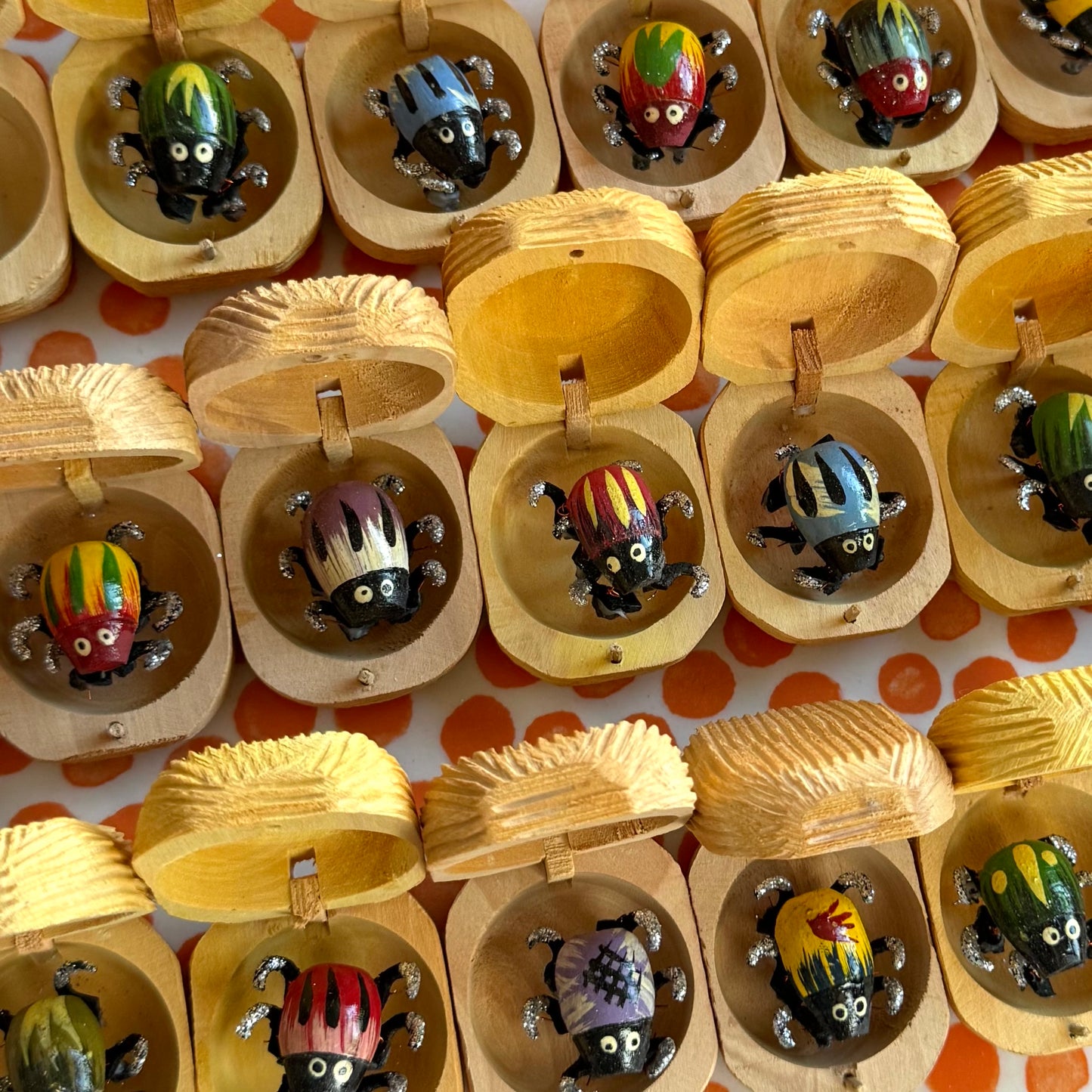 A bunch of Bug Nuts lined up, with a variety of colors and patterns. They all have six black legs covered with silver glitter, dangling beneath the body.