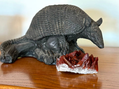 The specimen on a wood shelf in front of a decorative armadillo. In this lighting the color is a darker brick red, with good luster.