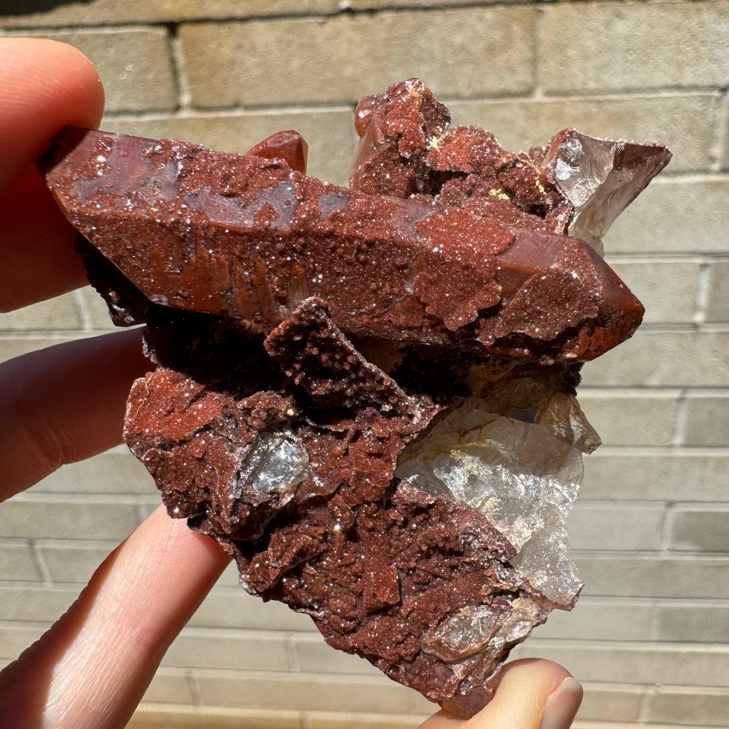 A red quartz point with glittering druzy patches on its surface, perched atop an irregular mass or colorless and red quartz.