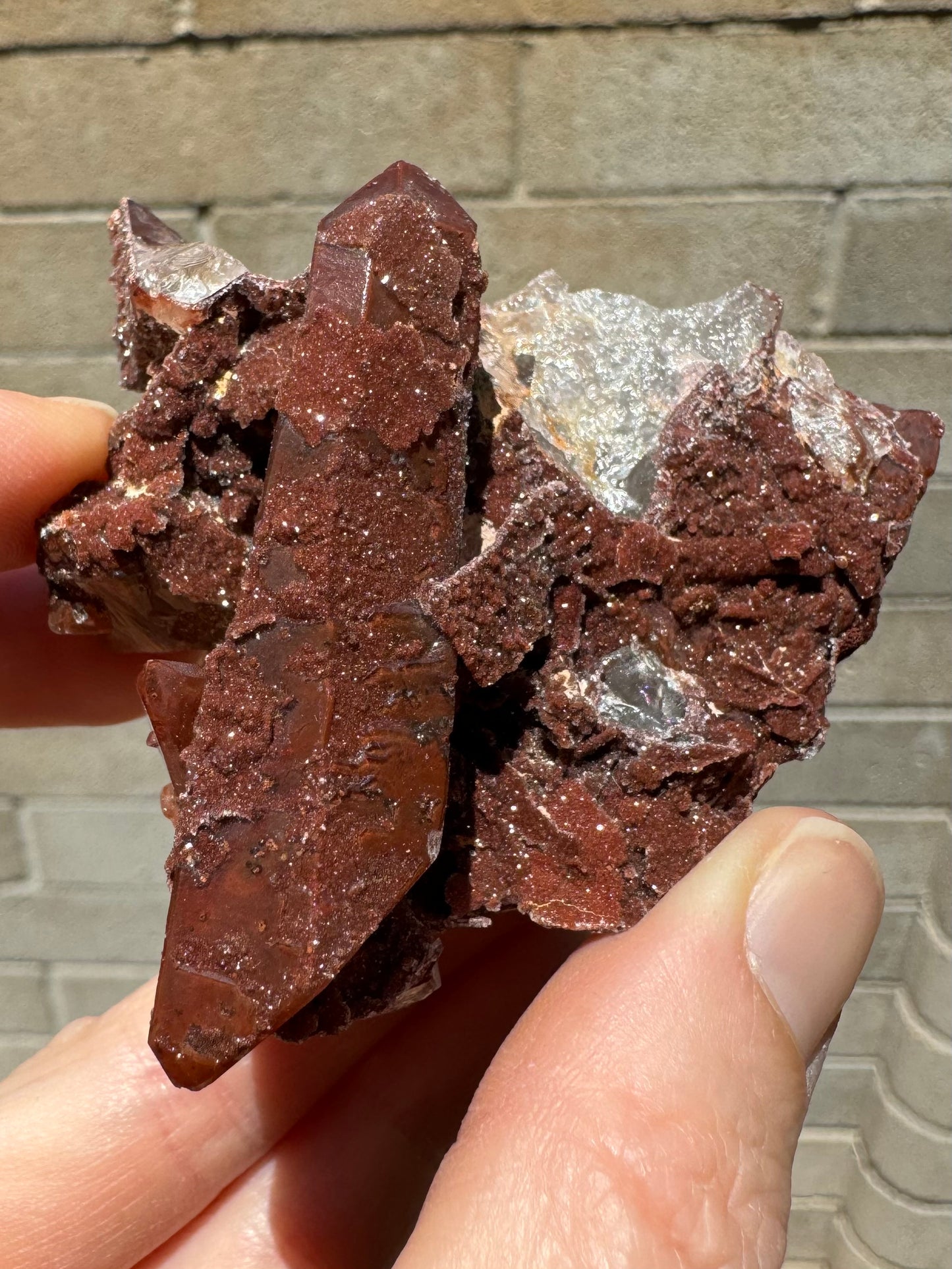 Close view of the specimen with the quartz point pointed up, and the surface texture visible. It is partially covered with druzy, an part clear with a red matte layer within.