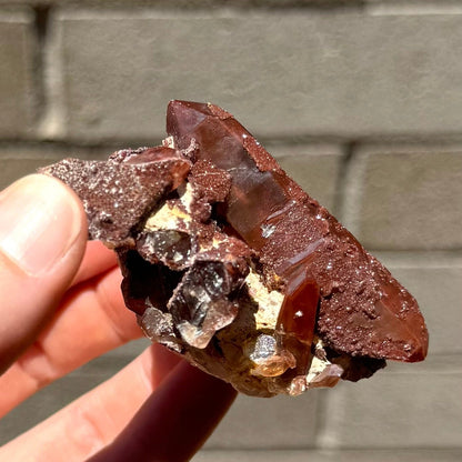 Side-view of the specimen, with a poor surface luster of the red quartz interruped by glittering druzy. Near the base, there is a well-formed small point with phantom coloring 