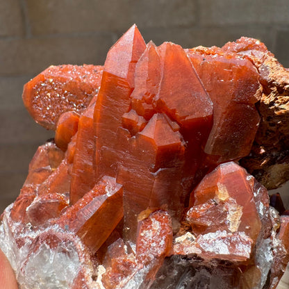 Detail of the cluster on the backside, multiple intersecting crystals with excellent growth forms and almost streaky appearing red coloration under the surface. The mineral is more clear on the surface, glowing orange.