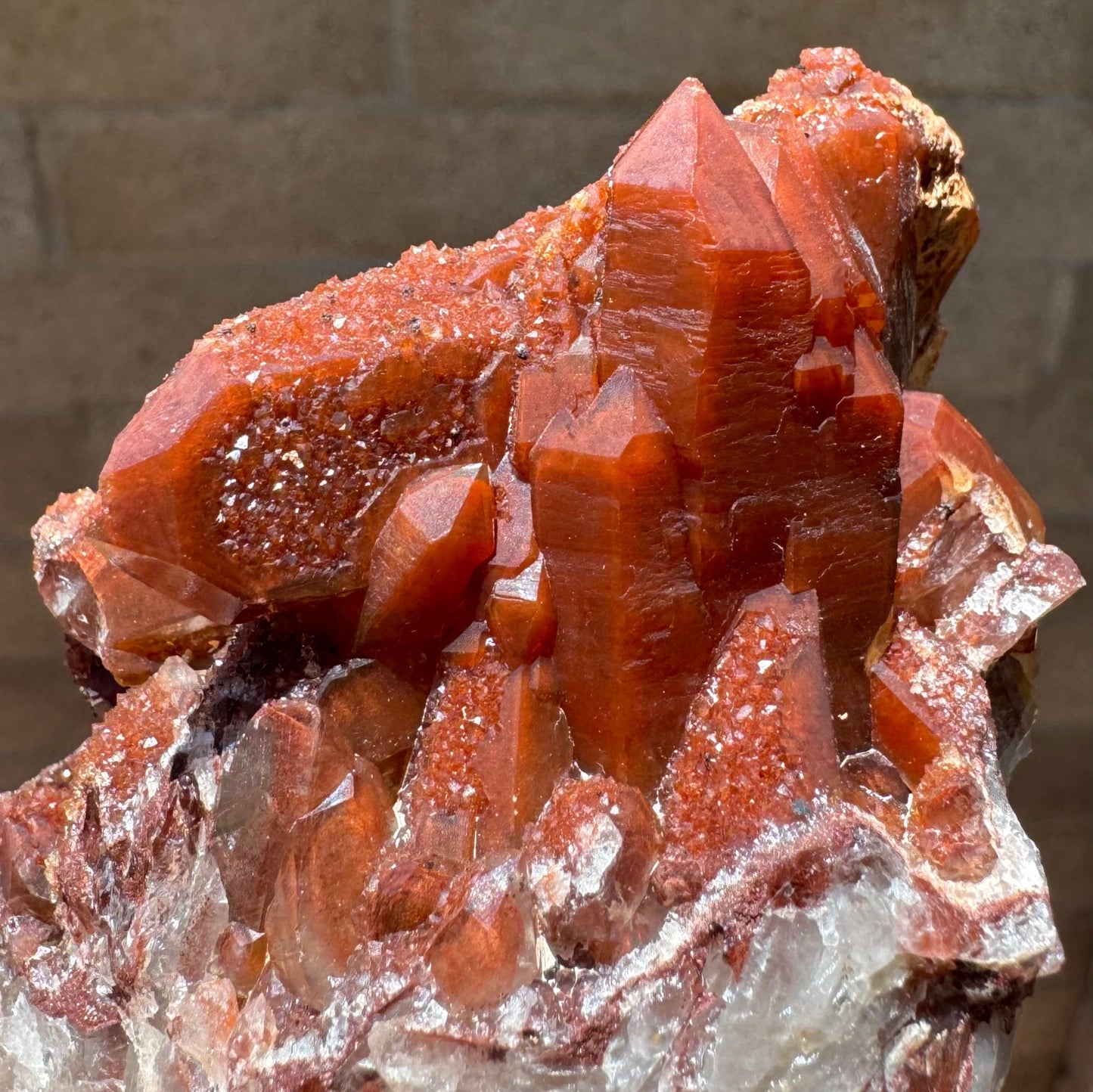 Detail of well-formed clustered peak growth of red quartz. A point on the other side is positioned behind them, oriented horizontally. Its main face is inverted with a druzy surface.