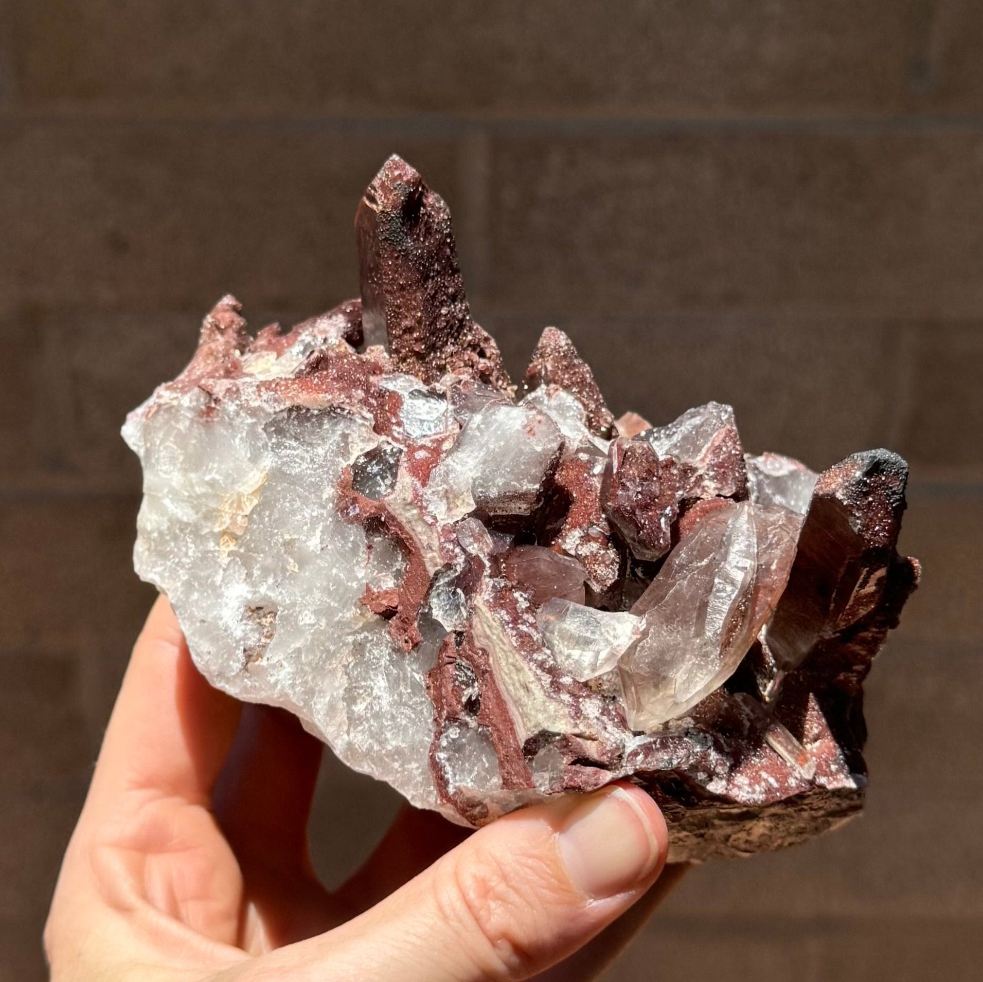 A side-view of the specimen, dark red-brown material atop a white quartz aggregate. Along the edge is a row of hexagonal shapes of broken quartz ringed by red hematite-included material.