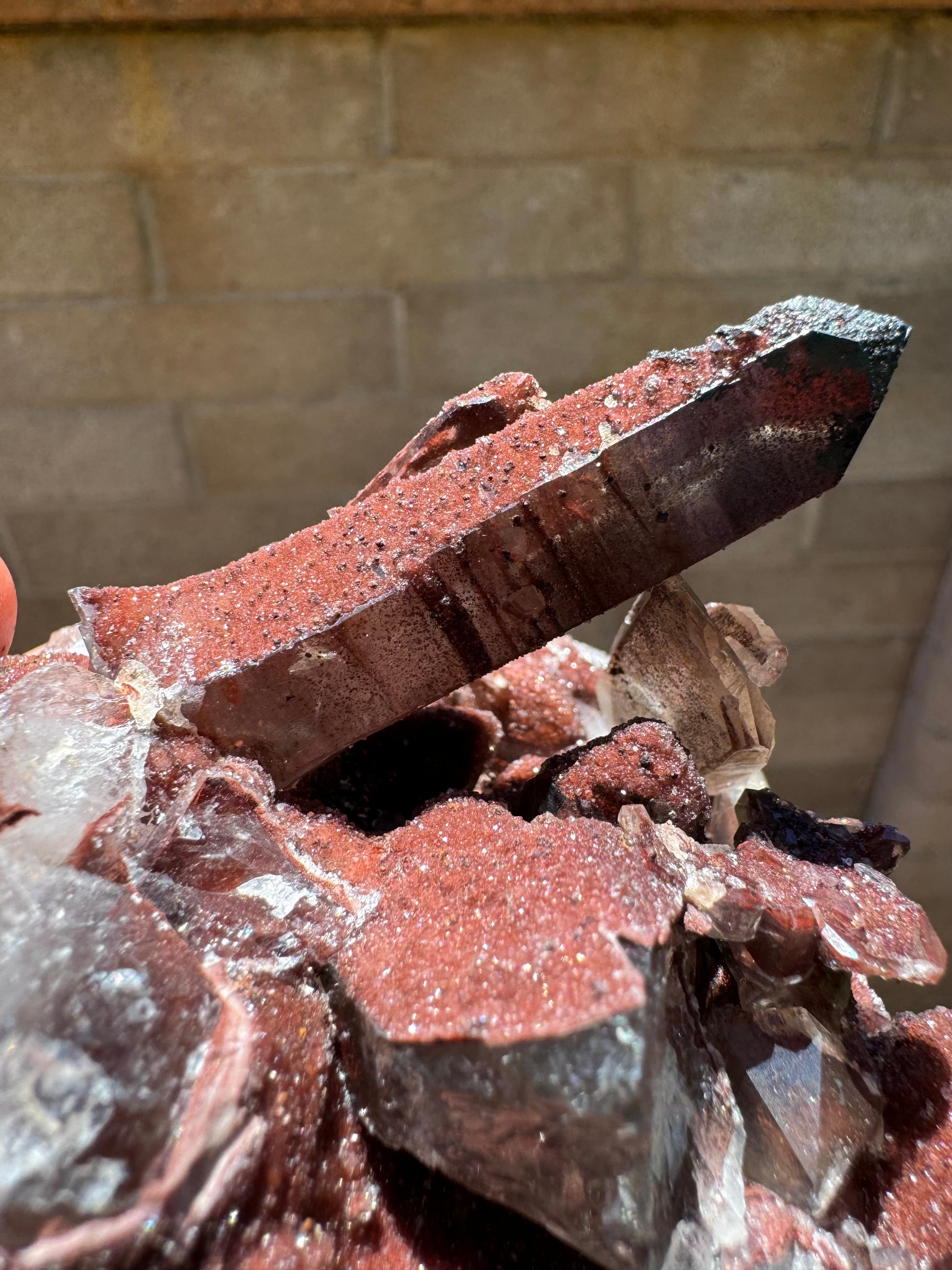 Another angle of the main point, showing the clarity through one side and the other side coated in glittering red druzy with small black dots.