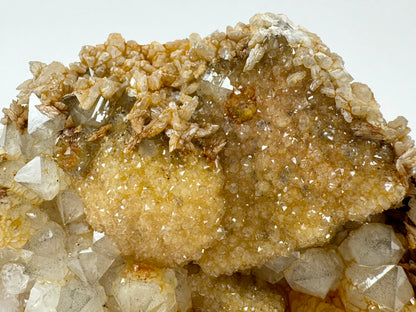 Detail of the larger cube and spherical formations covered with druzy, with a red ring of iron-staining. Reflecting quartz faces show clean growth. Calcite with poorer luster like brown rice grains covers the top of the mineral.