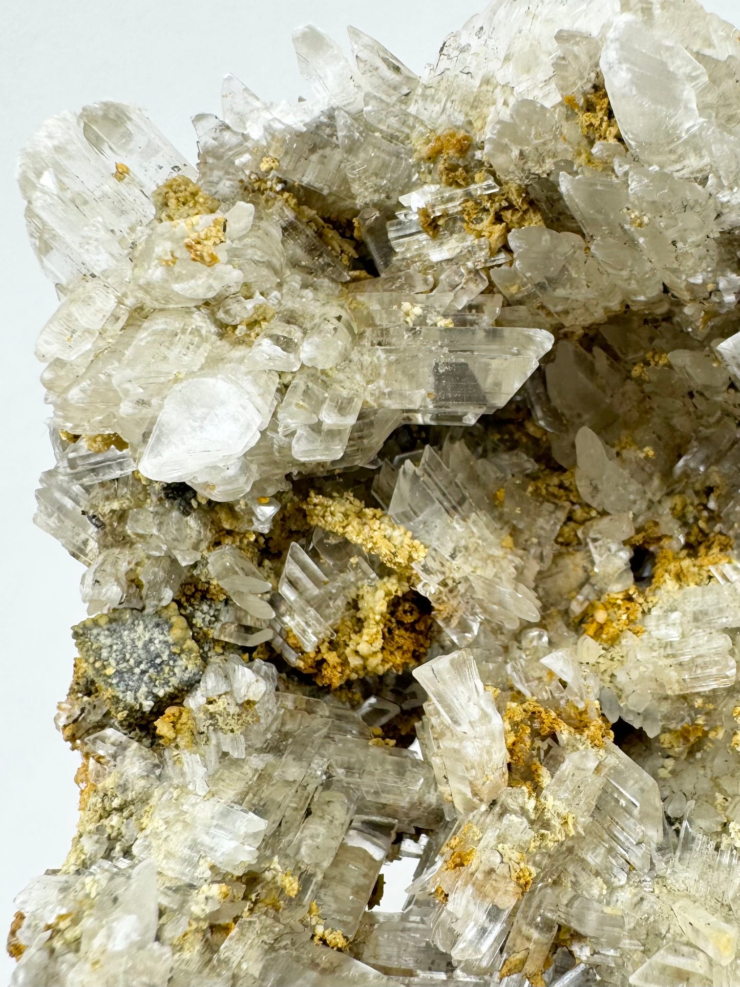 Detail of selenite crystals pointed in all directions. On the left edge is a small cube formation covered with light mineral.