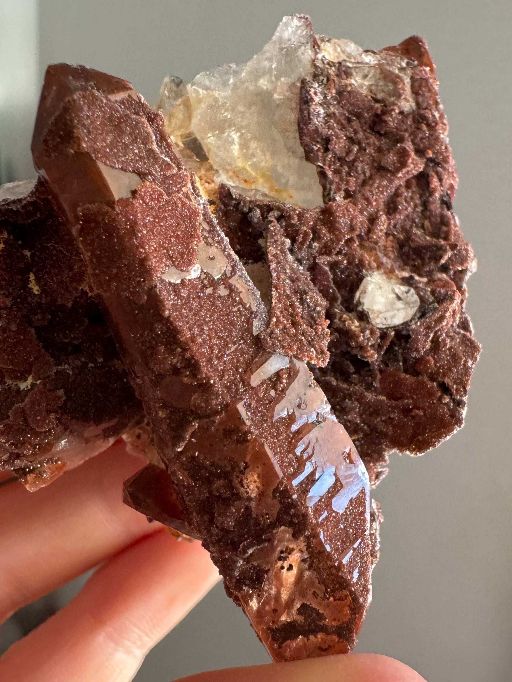 The quartz point tilted to reflect light, showing where the surface isn't shirt it is inverted and coated in a fine druzy. There is a crust of druzy on top of the point's surface near the tip.