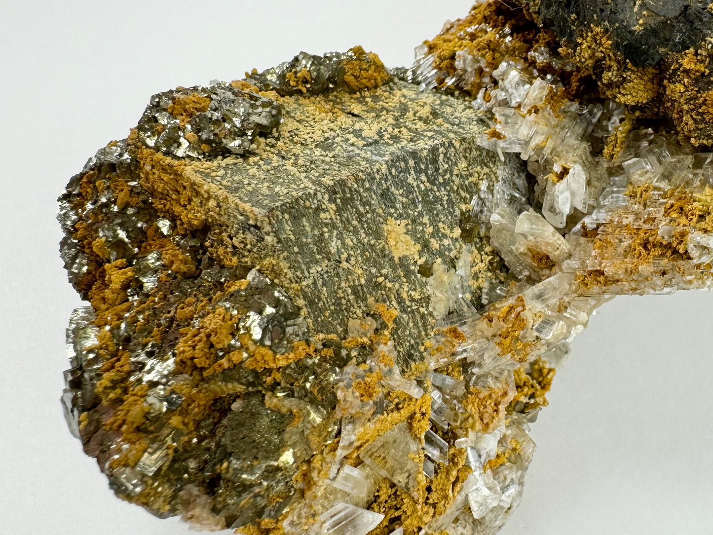 Detail of a large hexagonal barrel shaped mineral covered with other minerals, including small dots of yellow mineral along planes on the surface.