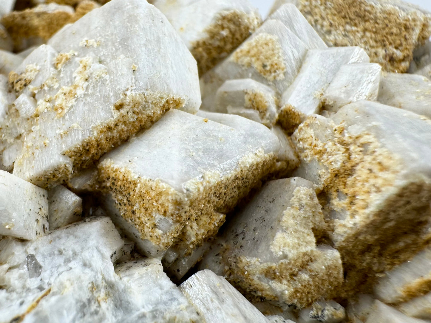 Detail of the mineral deposition on the surface of the microcline, a grainy tan like sand only on some sides of the white crystals.