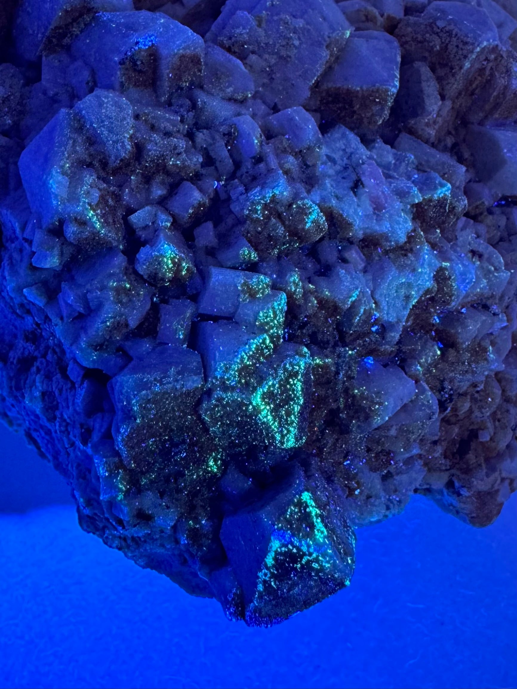 Detail of the mineral in the dark, exposed to UV light. The mineral fluoresces a light green color in small spots on the surface, which are mainly concentrated on the junctions between faces of the mineral.