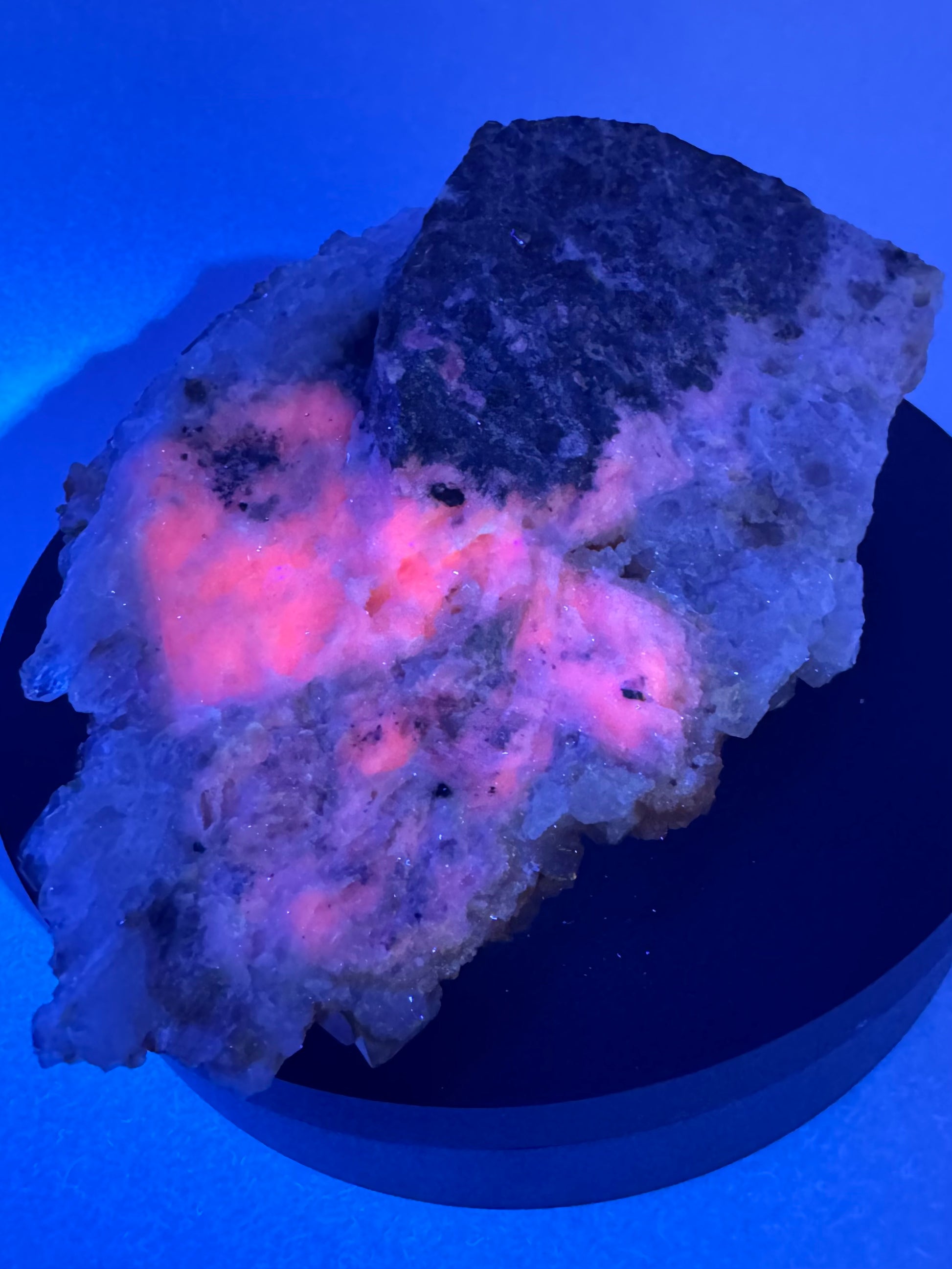 Bottom of the mineral specimen exposed to UV light, with the calcite fluorescing a peachy red color in the shape of two squares.