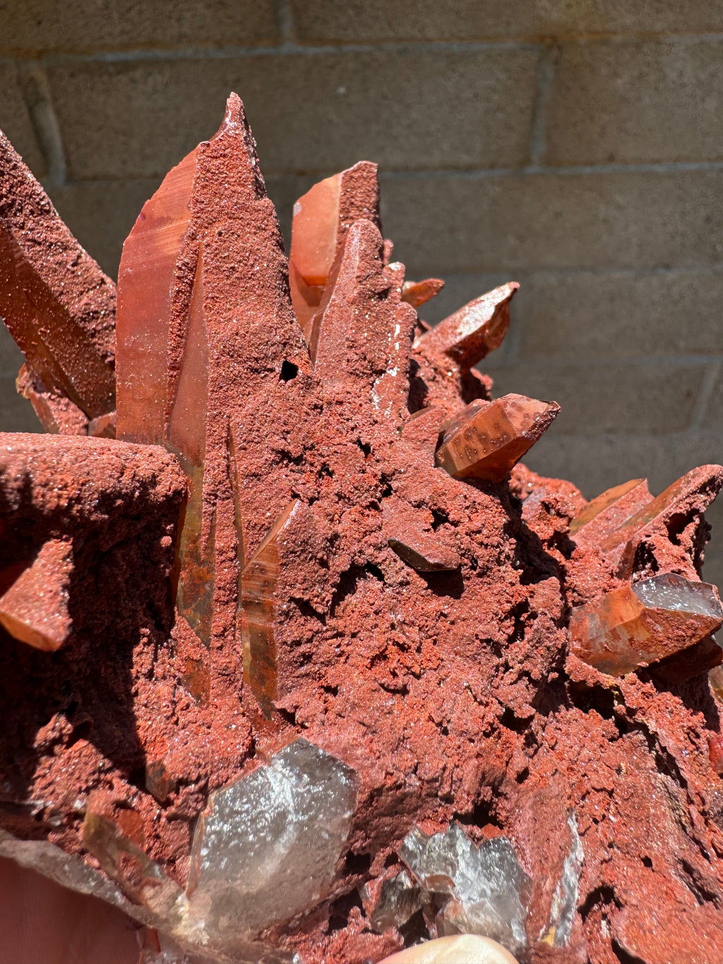 Detail of quartz points in the cluster, with one side coated in the bumpy opaque overgrowth, which is matte with a slight glitter like sand. The bare side is red quartz with tones of orange and yellow in laces.