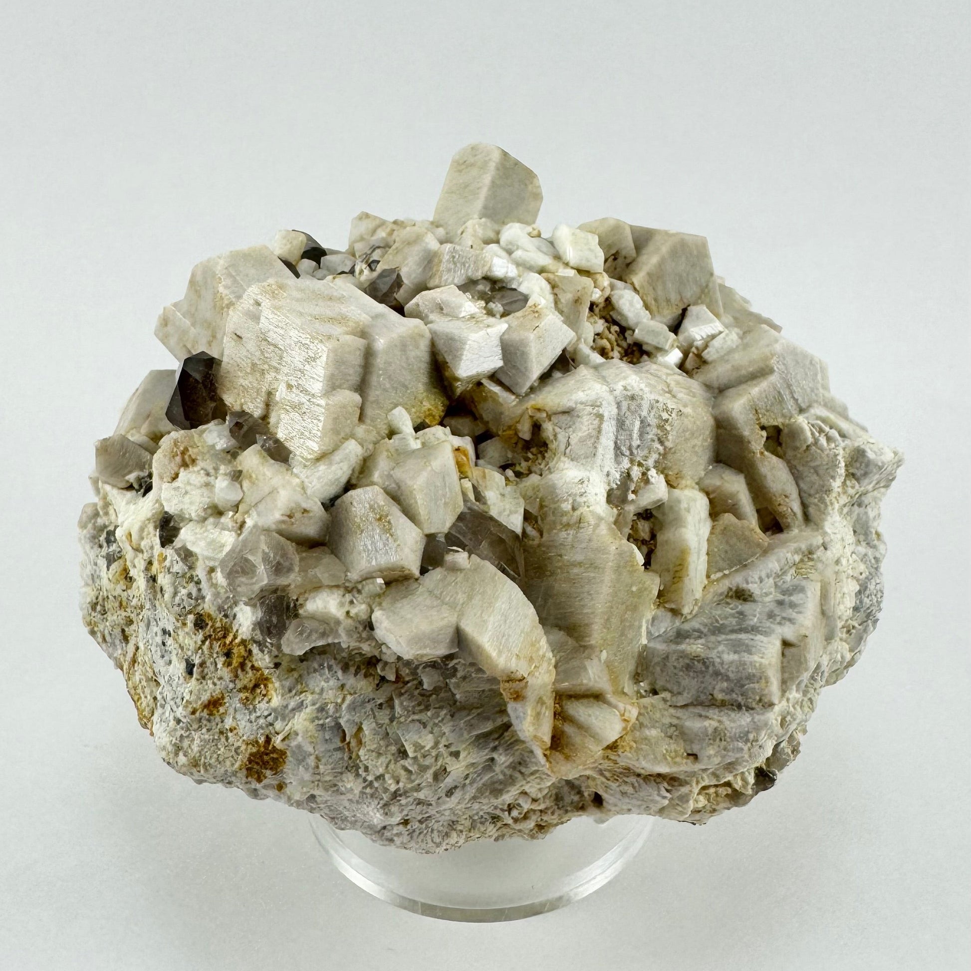 Full view of the mineral specimen, a rough base with the front covered with large blocky microcline crystals. One rectangular block extends tall out of the specimen. Several smoky quartz crystals are visible.