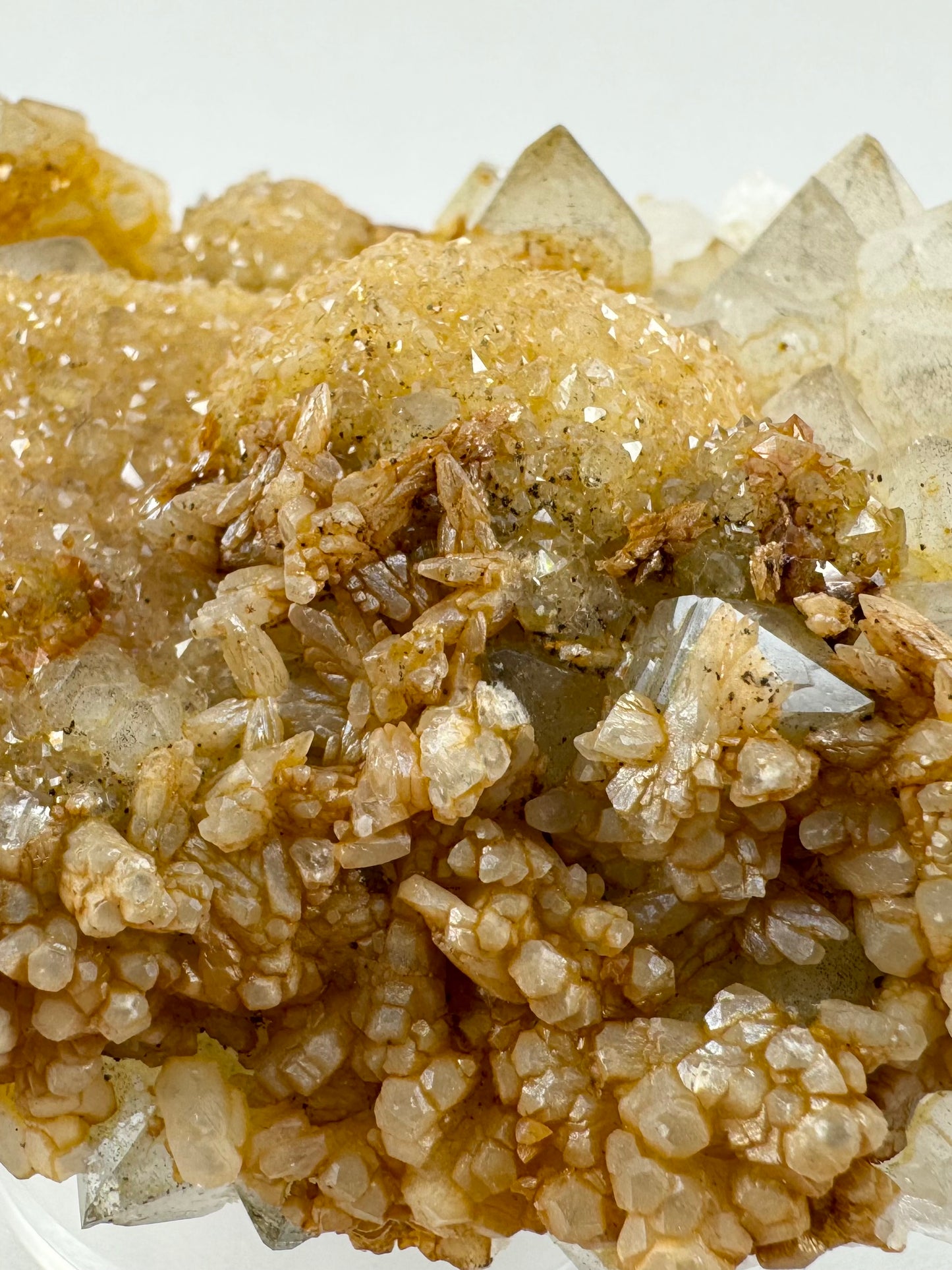 Detail of the side of the specimen, displaying multiple growth types at once. The top of the specimen is covered with druzy with quartz points on the right. In the foreground the specimen is covered in rice-grain-like calcite crystals that devolve into hexagonal crystals.