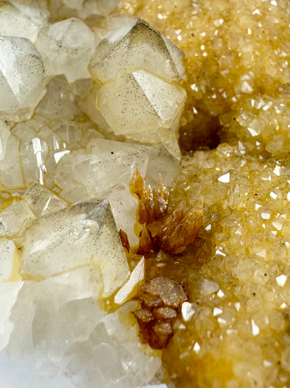 Detail of a cluster of steep dogtooth calcite points on the edge between the light brown-yellow druzy on the right and the larger white quartz crystals on the left.