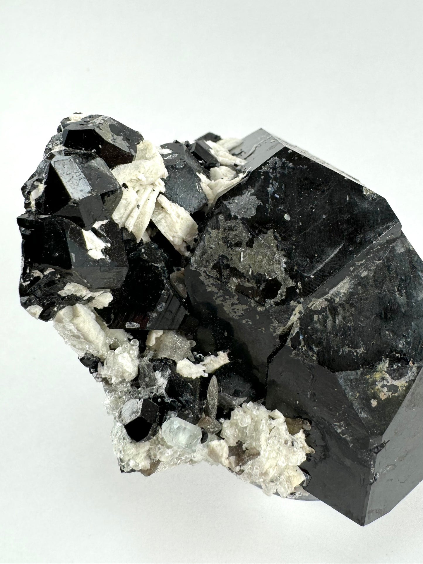 The specimen in the same position as the previous photo, in plain white light. The fluorescent colorless hyalite was mostly covered white albite. A good mercedes termination is visible on one of the smaller schorl crystals, with a small pale aquamarine crystal near it.