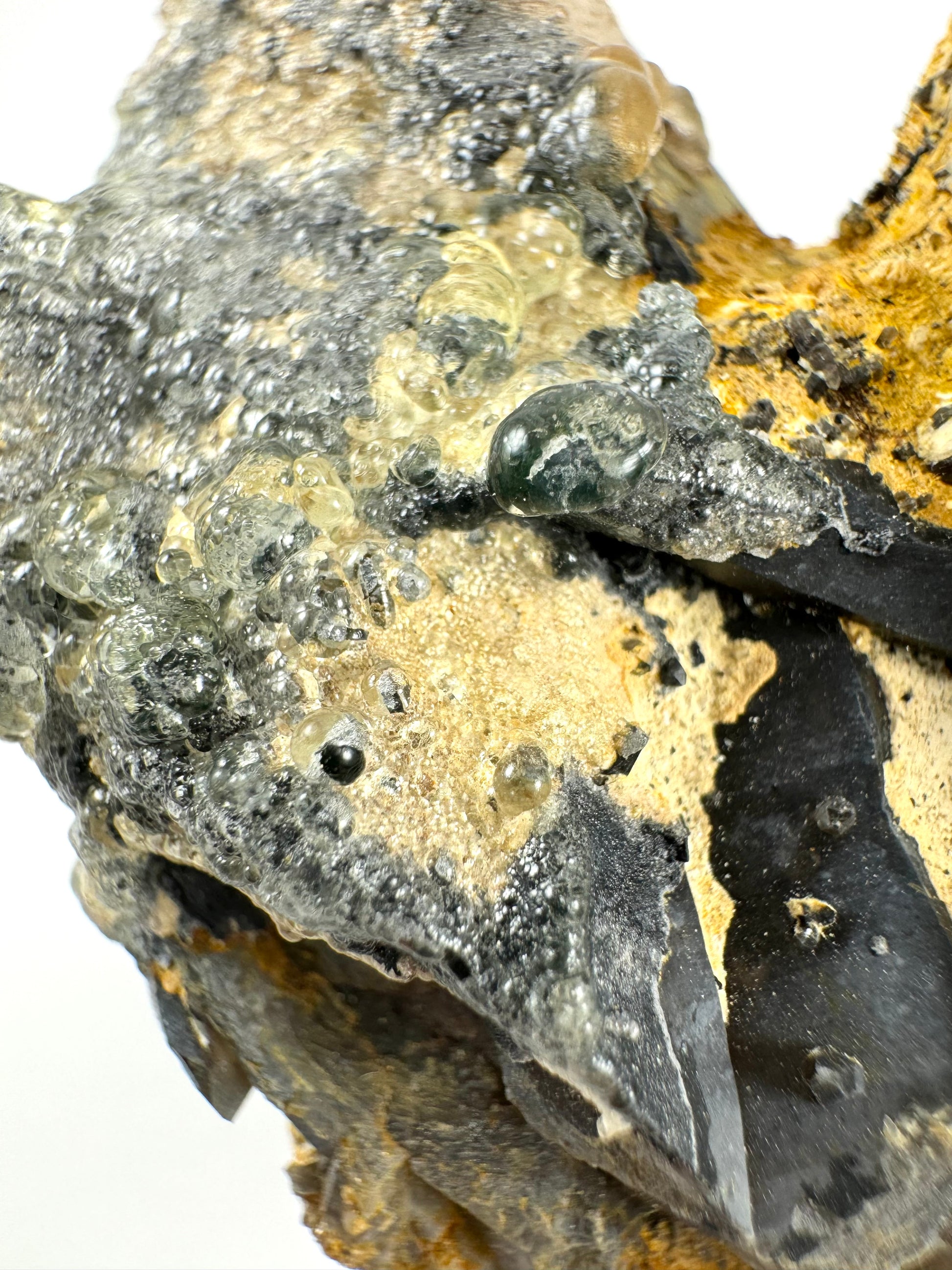 The first of two lighting images: detail of shard-like pieces of smoky quartz on the specimen covered with thick hyalite forming large colorless spheres with high luster, looking like bubbles on the surface.