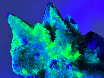 The piece in the same position as the previous image, in the dark and illuminated with blue-tinted UV light. The hyalite fluoresces a strong yellowish-green in the thicker growth and light blue in the thinner hyalite.