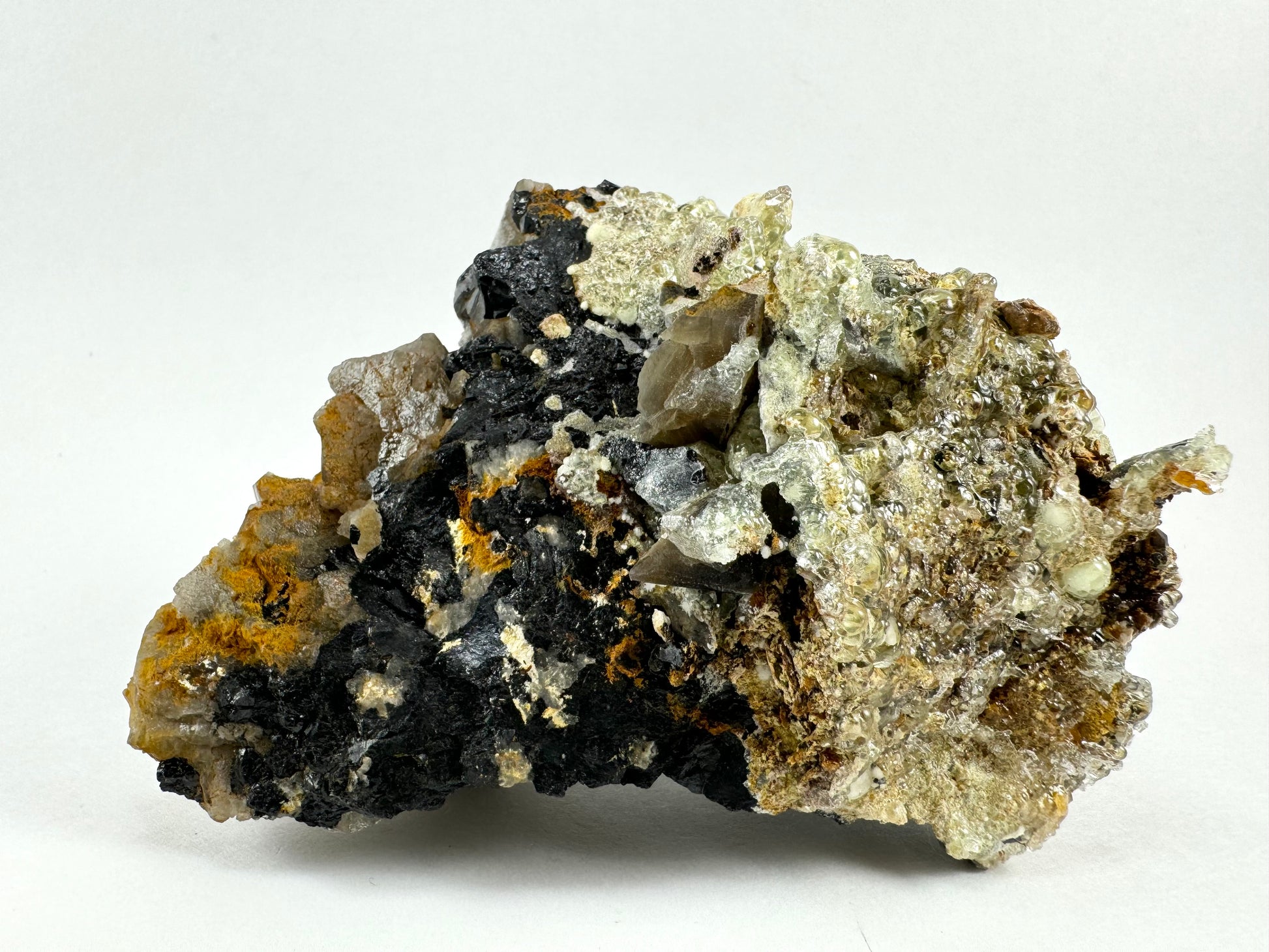 The bottom of the specimen, an aggregate of irregular schorl crystals with shards of smoky quartz. The right side is coated with large botryoidal hyalite with high luster reflecting like bubbles. There are two large spheres of hyalite on the far right that are white and opaque like snowballs instead of glassy.