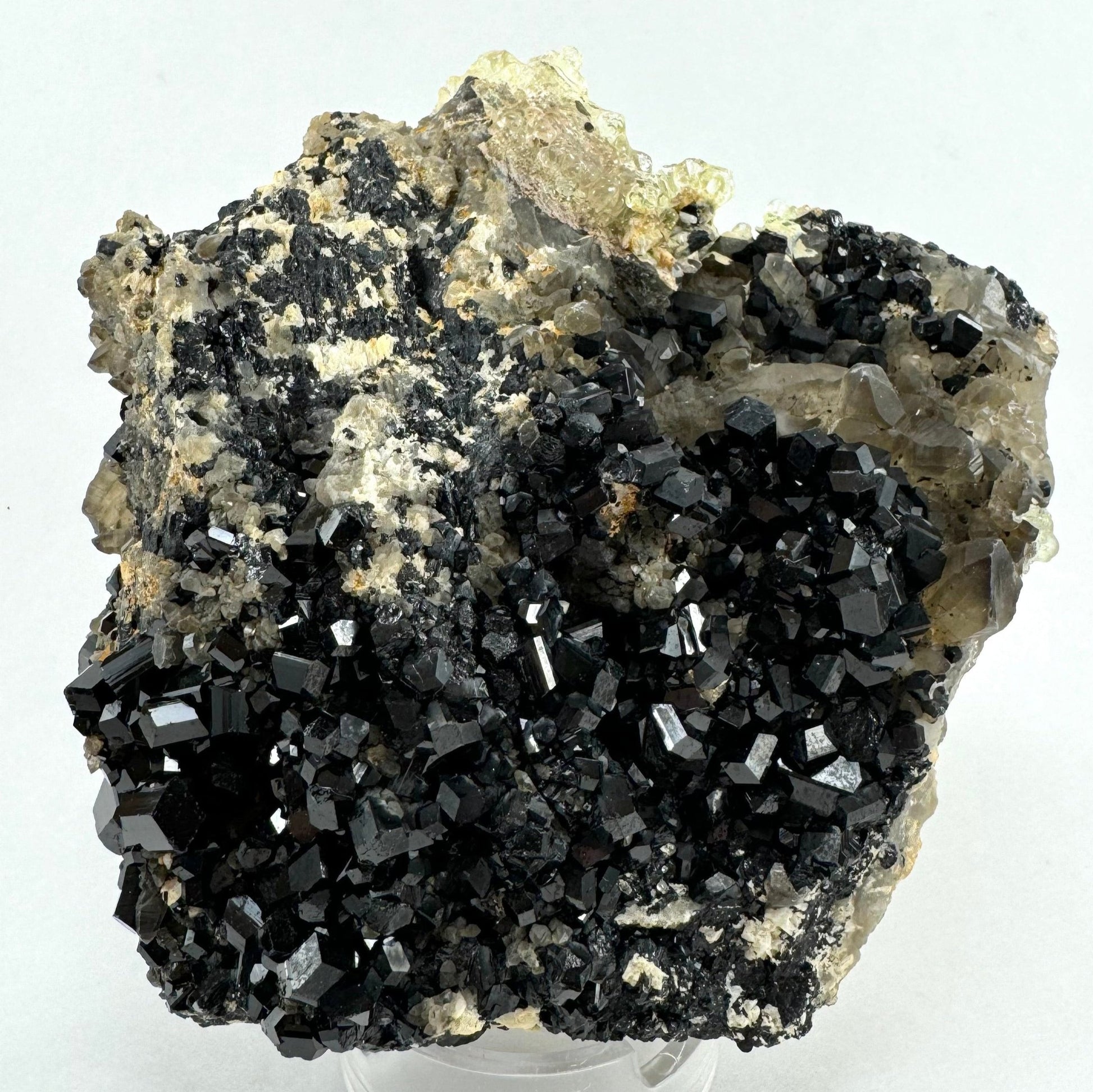 A tapered square-shaped specimen, over half covered with lustrous schorl crystals with a cluster of smoky quartz in the upper right. The top left is a rough aggregate matrix of schorl and white albite.