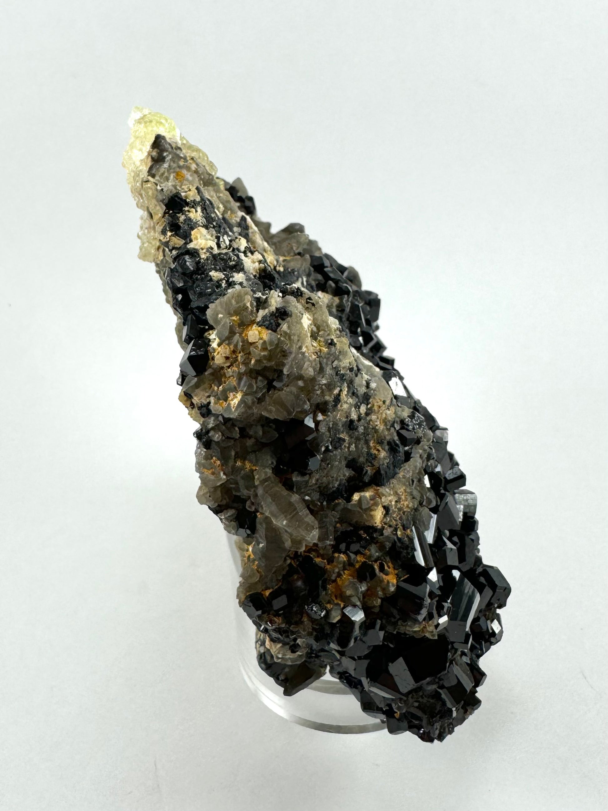 Side-view of the specimen, wedge-shape with a wide base thick with schorl and a thin top crested with hyalite. There are several smoky quartz crystals on the back side of the edge.