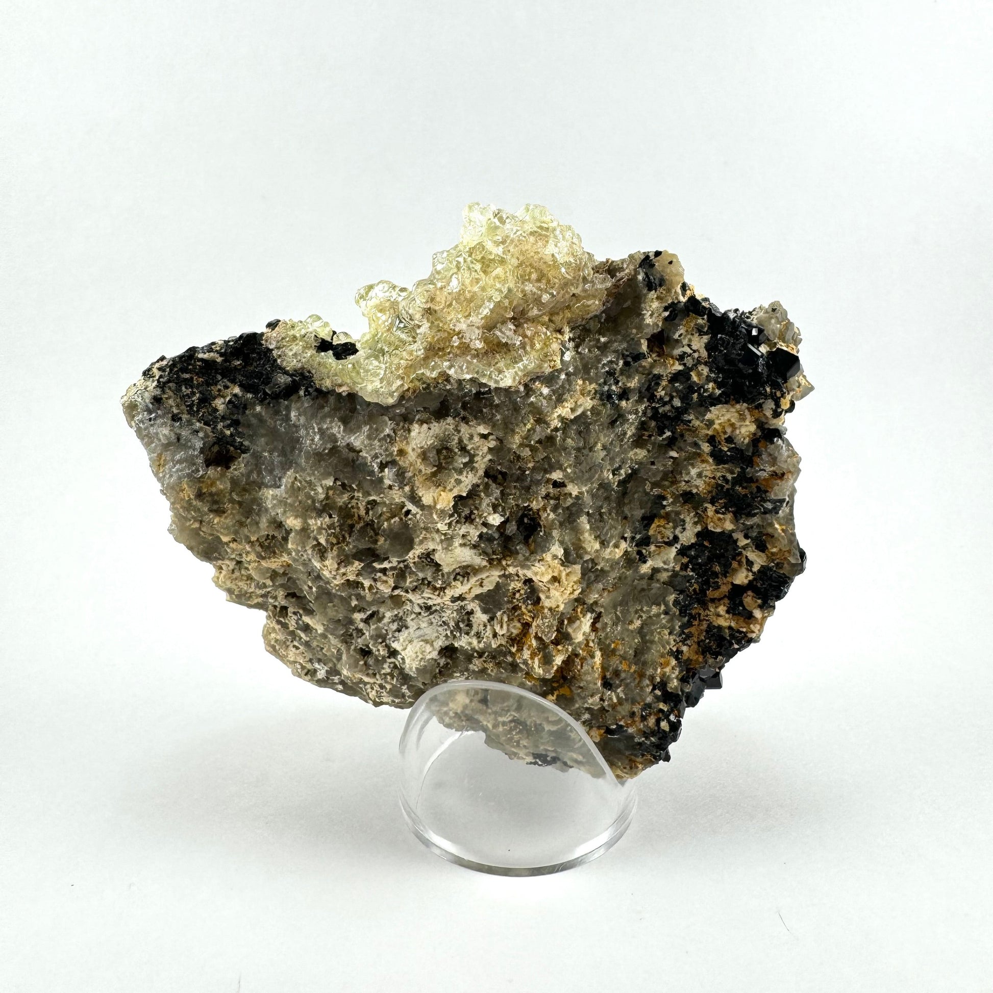 The back of the specimen, a rough aggregate matrix that appears composed of smoky quartz, albite, and schorl. There is a light yellow splash-like hyalite formation on the top.