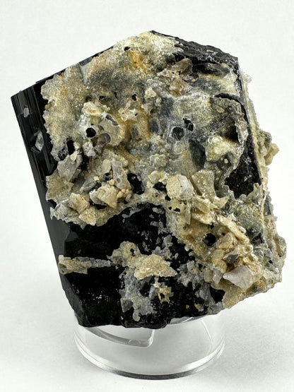 An angled view of the side of the specimen covered with hyalite, with shards of white albite trapped in the mass. There are two inverted hexagons in the left edge of the schorl, with hyalite in the bottom.