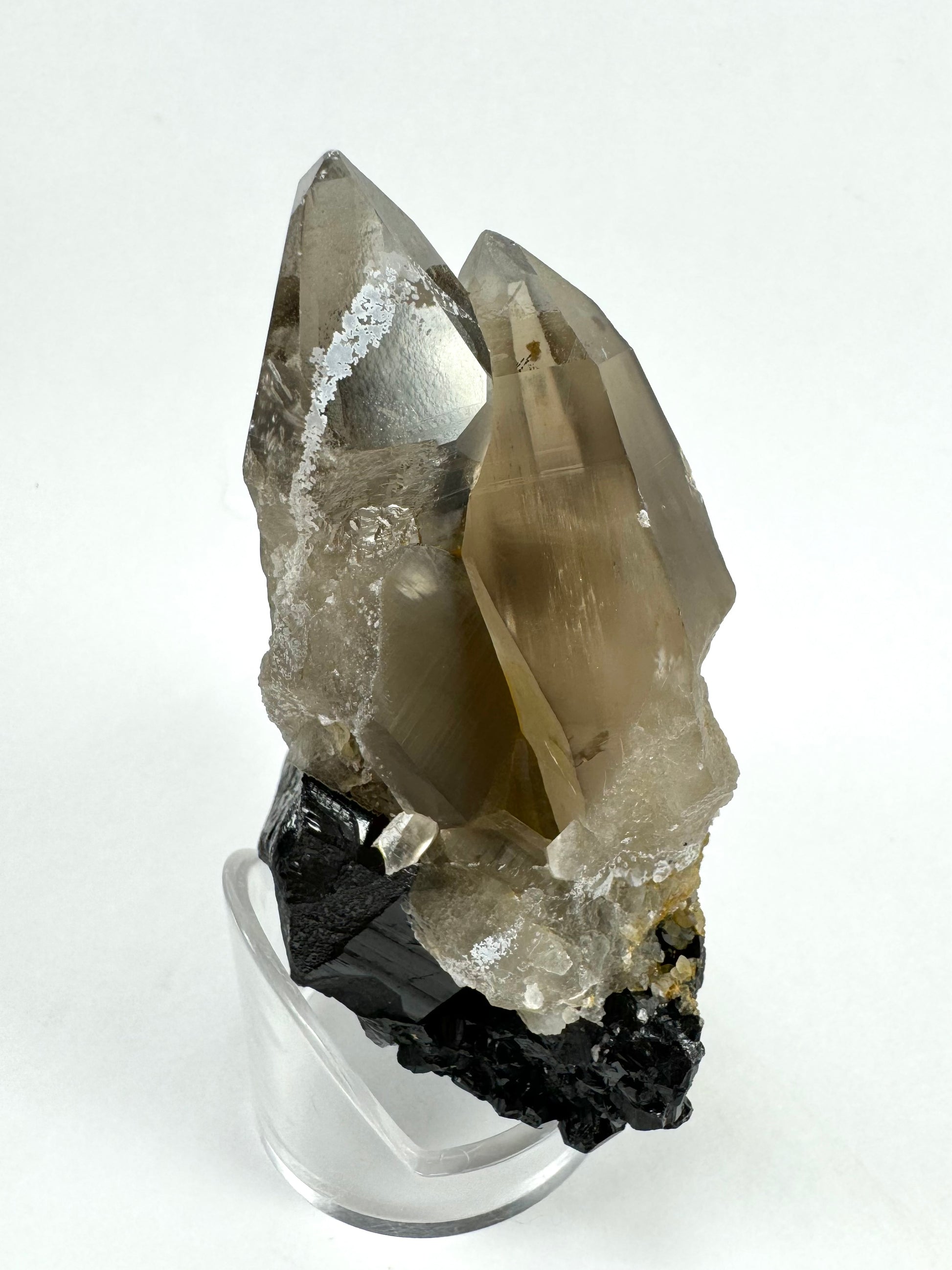 The side of the smoky quartz . The broad face of the larger point is reflecting light, highlighting a ripple-like pattern on the surface. The smaller point is bright as though inclusions are catching light.