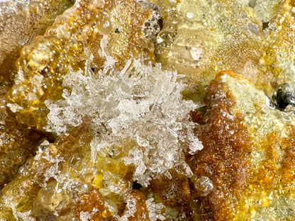 Close detail of the rounded cluster of needles on the mineral, colorless but appearing white due to their small size. The needles melt into botryoidal growth, with large and small spheres with high luster.
