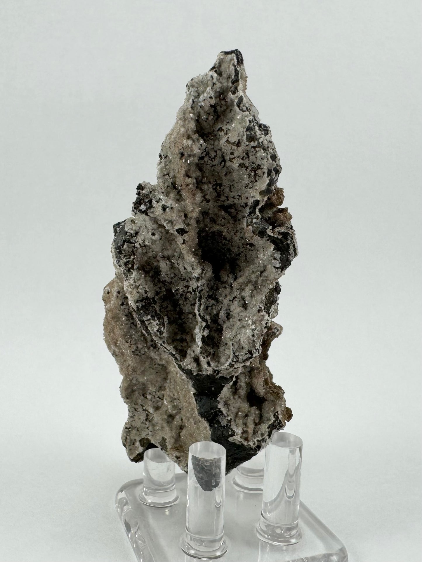 The back side of the specimen, with near-black matrix craggy with deep pockets. It is coated in off-white druzy with better glitter without the brown lizardite overcoating. 