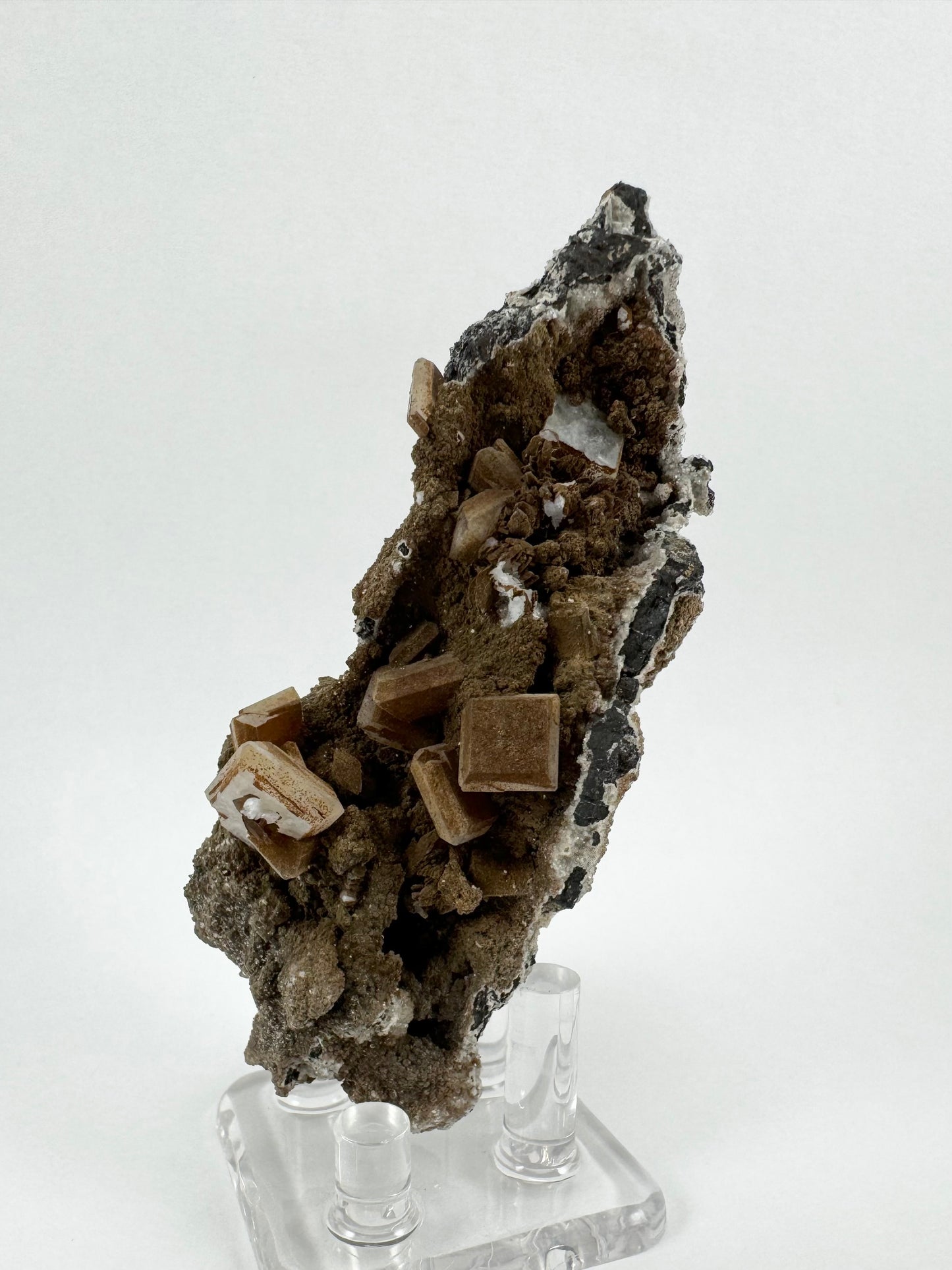 A long skinny mineral specimen with square tabular crystals on matrix and coated in a brown mineral.