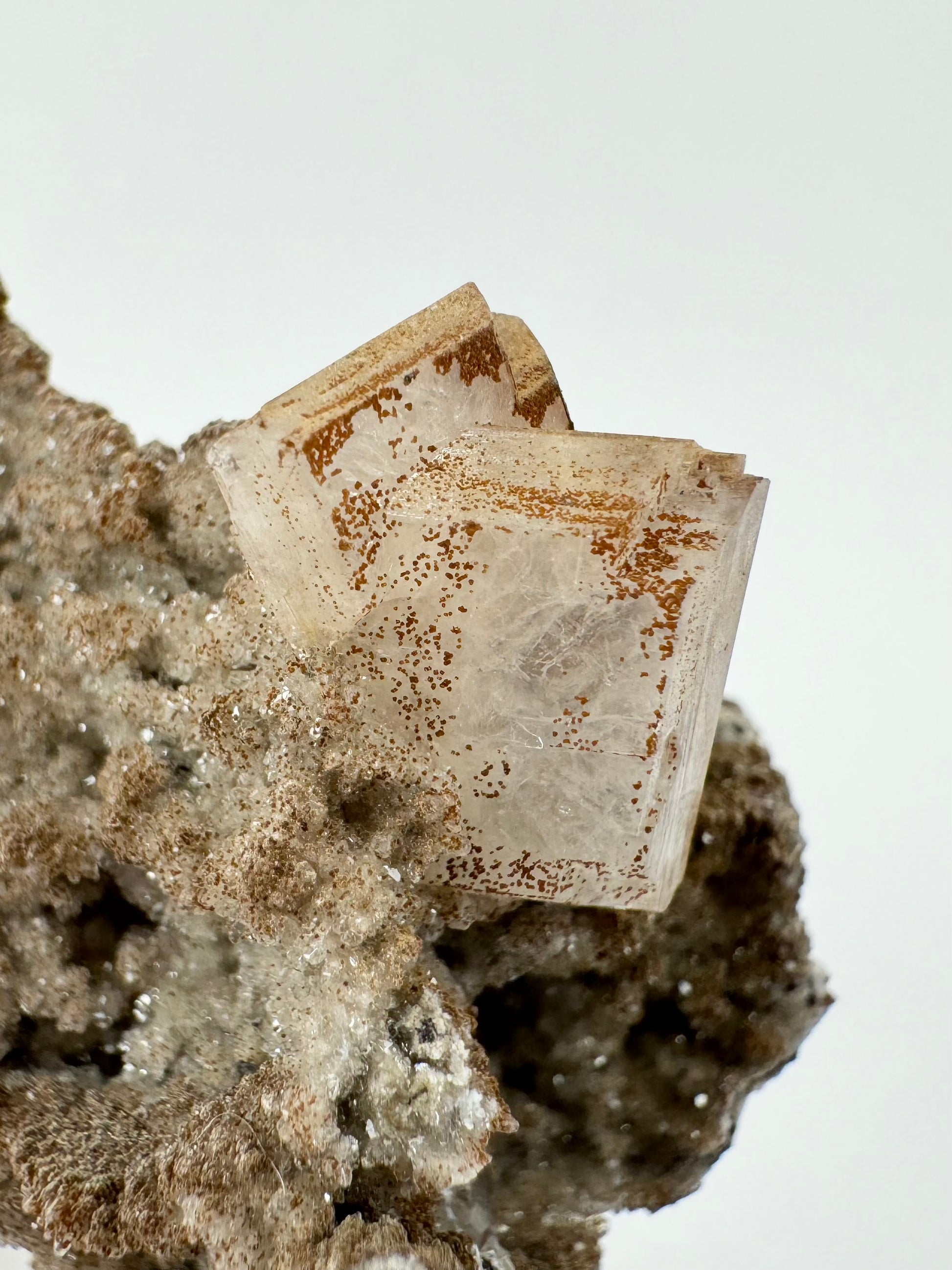 Detail of two intersecting hydroxyapophyllite crystals with spots of brown lizardite following the angular faces. The crystals are of a shiny calcite druzy