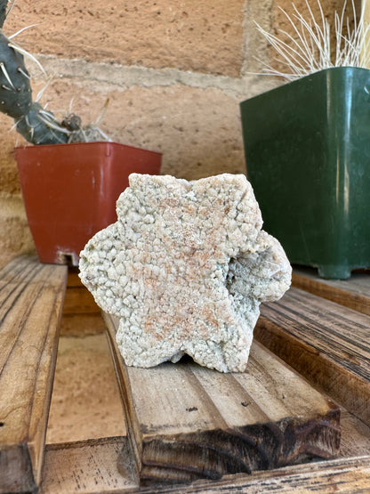 The piece on edge, closer view showing the side opposite from the mineral cluster. One of the six arms of the snowflake is not fully formed, stepping down a level at that corner. The piece has a brick-red color dusted over the surface.