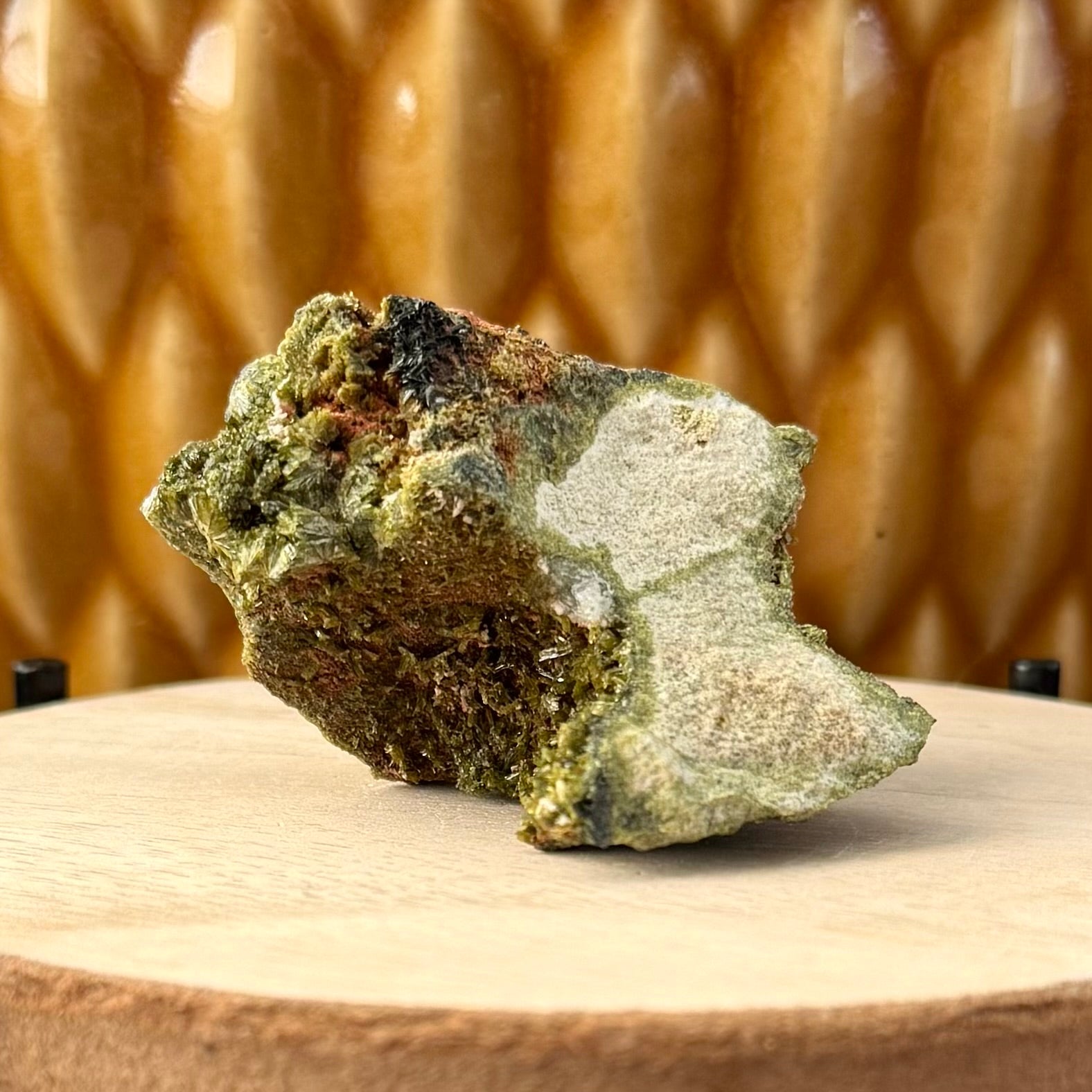 An irregular wedge-shaped piece of matrix with sides curved in, and epidote lining the near side and top. The front face is a light grainy matrix tinted green at the edges.