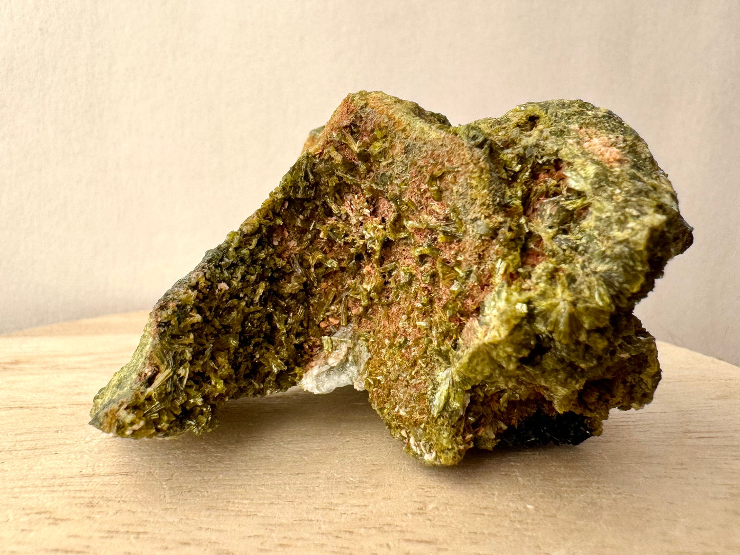 Close view of the other concave end of the specimen, a red-brown matrix covered with epidote crystals oriented in different directions.