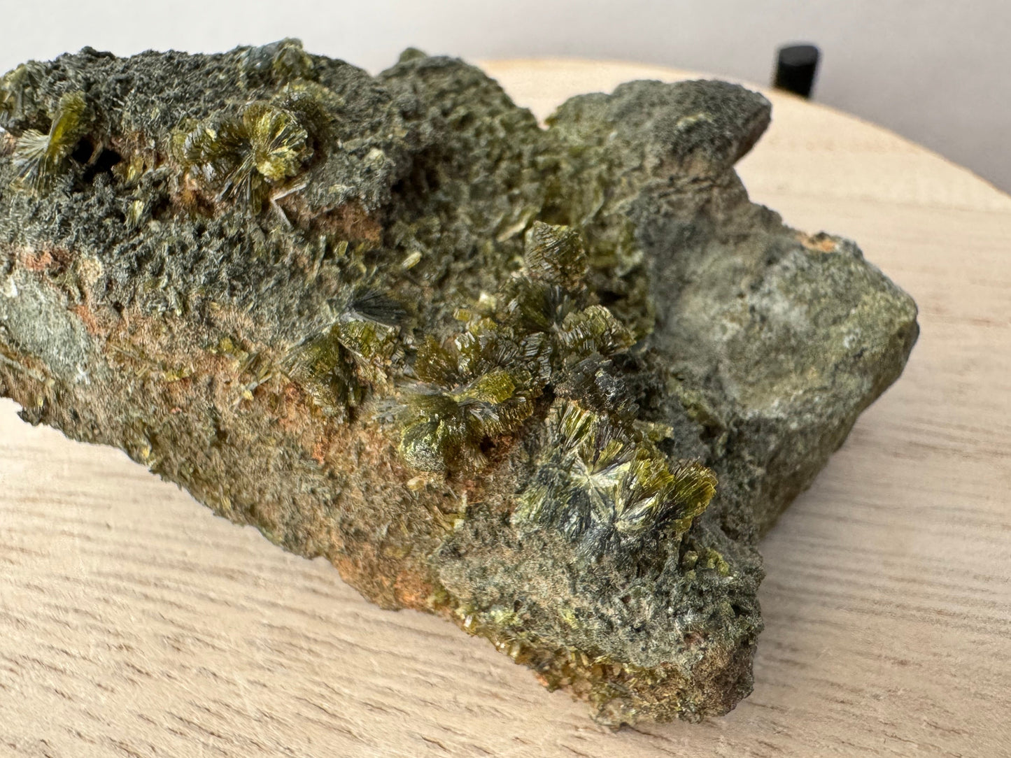 Detail of an edge of the specimen with a cluster of partial spheres of epidote crystals. The orange-brown matrix pokes through the dark layer of low-quality crystals